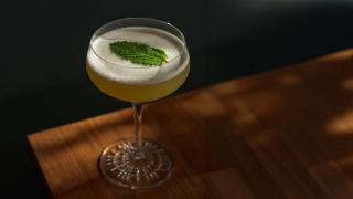 Gul drink pyntet med mynteblad, servert i coupe-glass