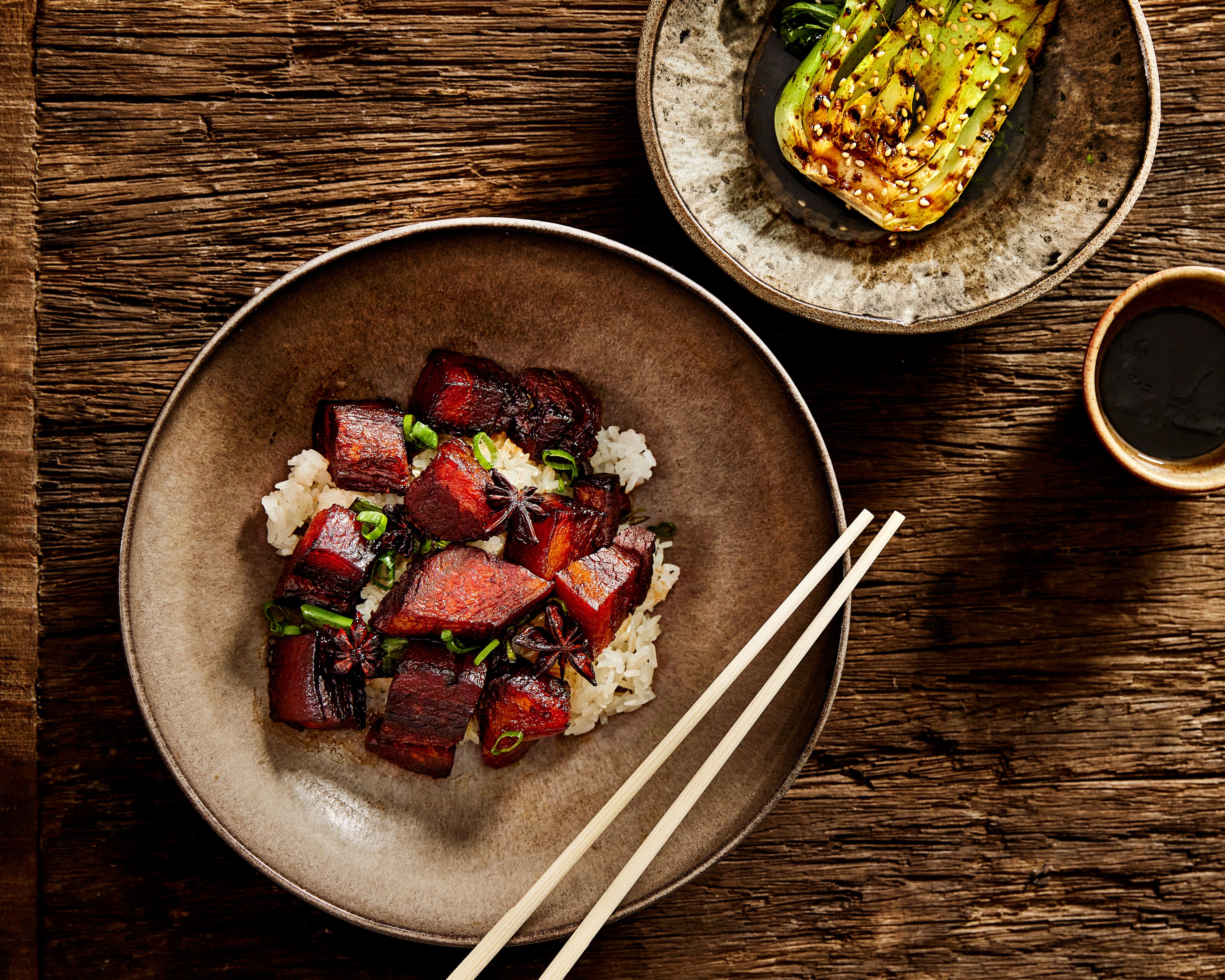 Tallerken med kinesisk karamellisert ribbe og ris, skål med soya og pac choi ved siden av.