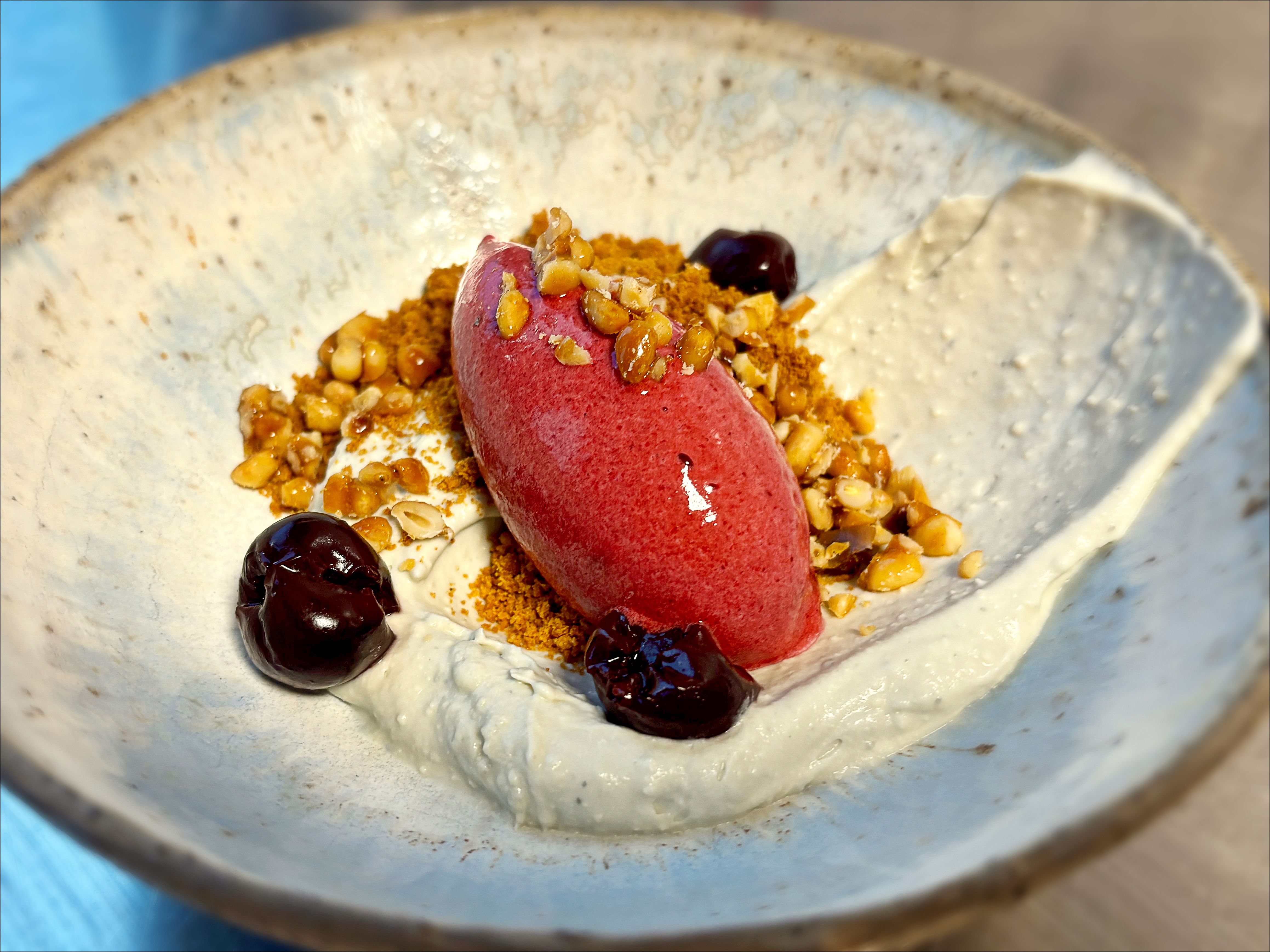 Skål med blåmuggostkrem, pepperkakesmuler, kirsebærsorbet og syltede kirsebær.