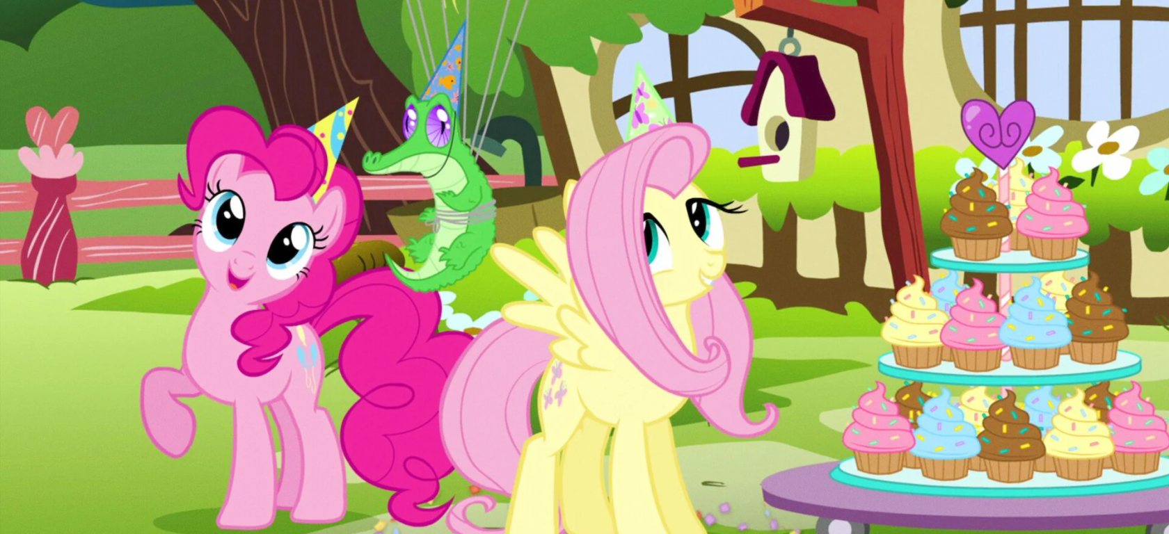 Fluttershy and Pinkie Pie share a quiet moment beside cupcakes