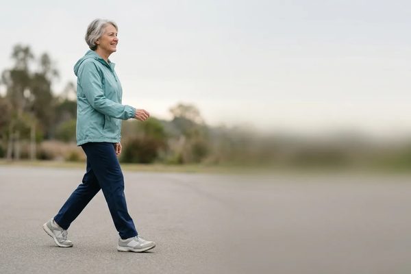 A woman in her late sixties walking on a park path in cushioned grey walking shoes.