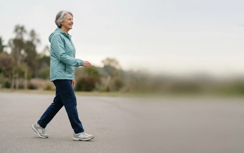 A woman in her late sixties walking on a park path in cushioned grey walking shoes.