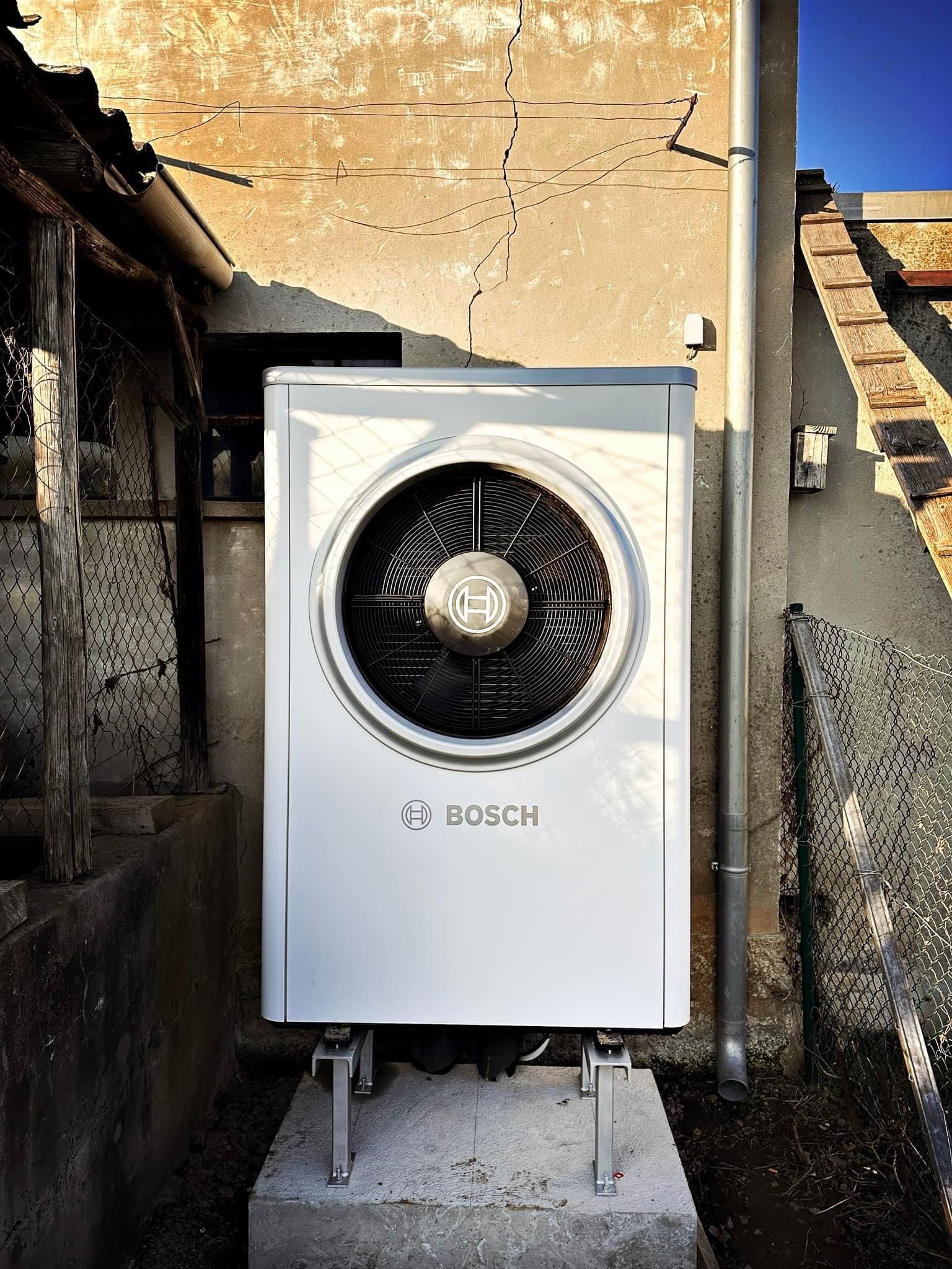 Außeneinheit einer Bosch-Wärmepumpe auf einem Betonsockel zwischen zwei Gebäuden