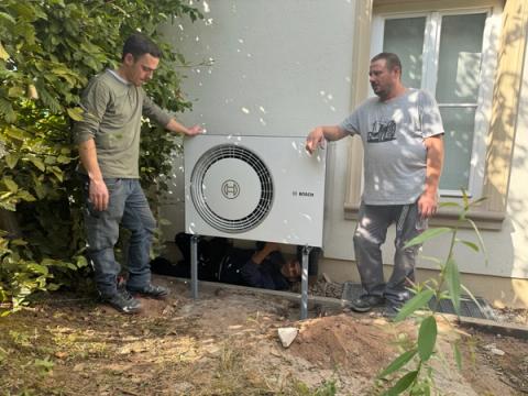 Zwei Männer neben der neu aufgestellten Außeneinheit einer Bosch-Wärmepumpe im Garten