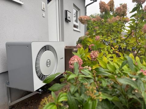 Außeneinheit einer Bosch-Wärmepumpe auf einer Wandkonsole neben blühenden Hortensien