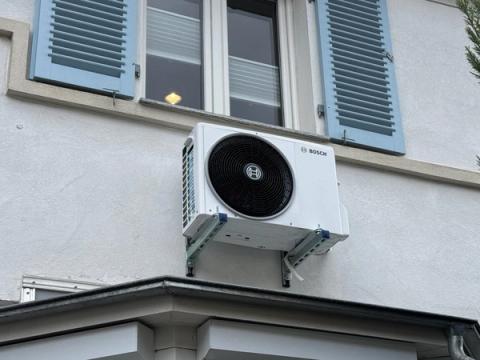 Bosch-Außengerät einer Klimaanlage auf einer Wandkonsole unter einem Fenster mit Fensterläden