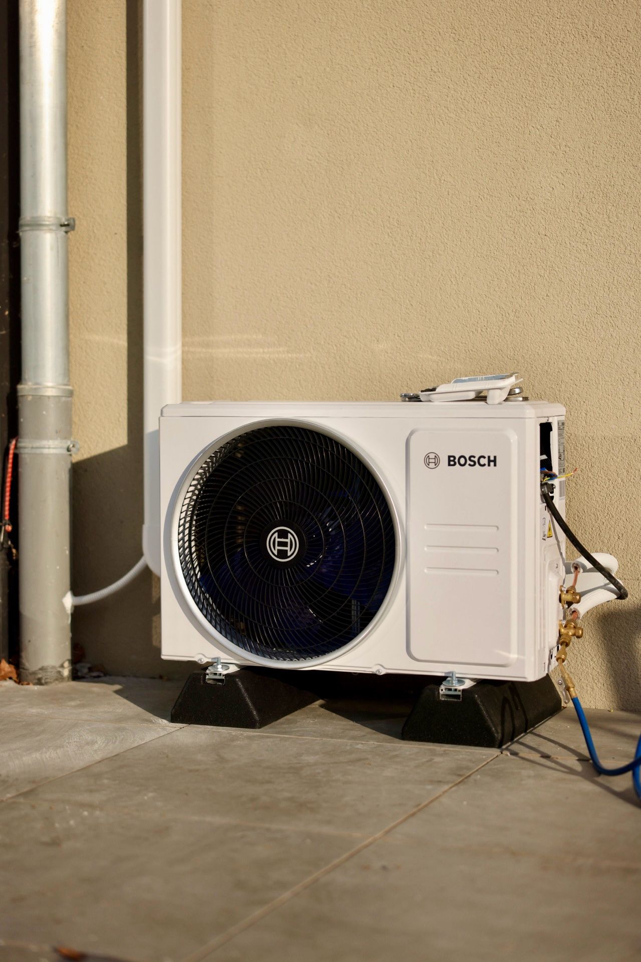 Bosch-Außengerät einer Klimaanlage auf Bodenfüßen vor einer beigen Hauswand