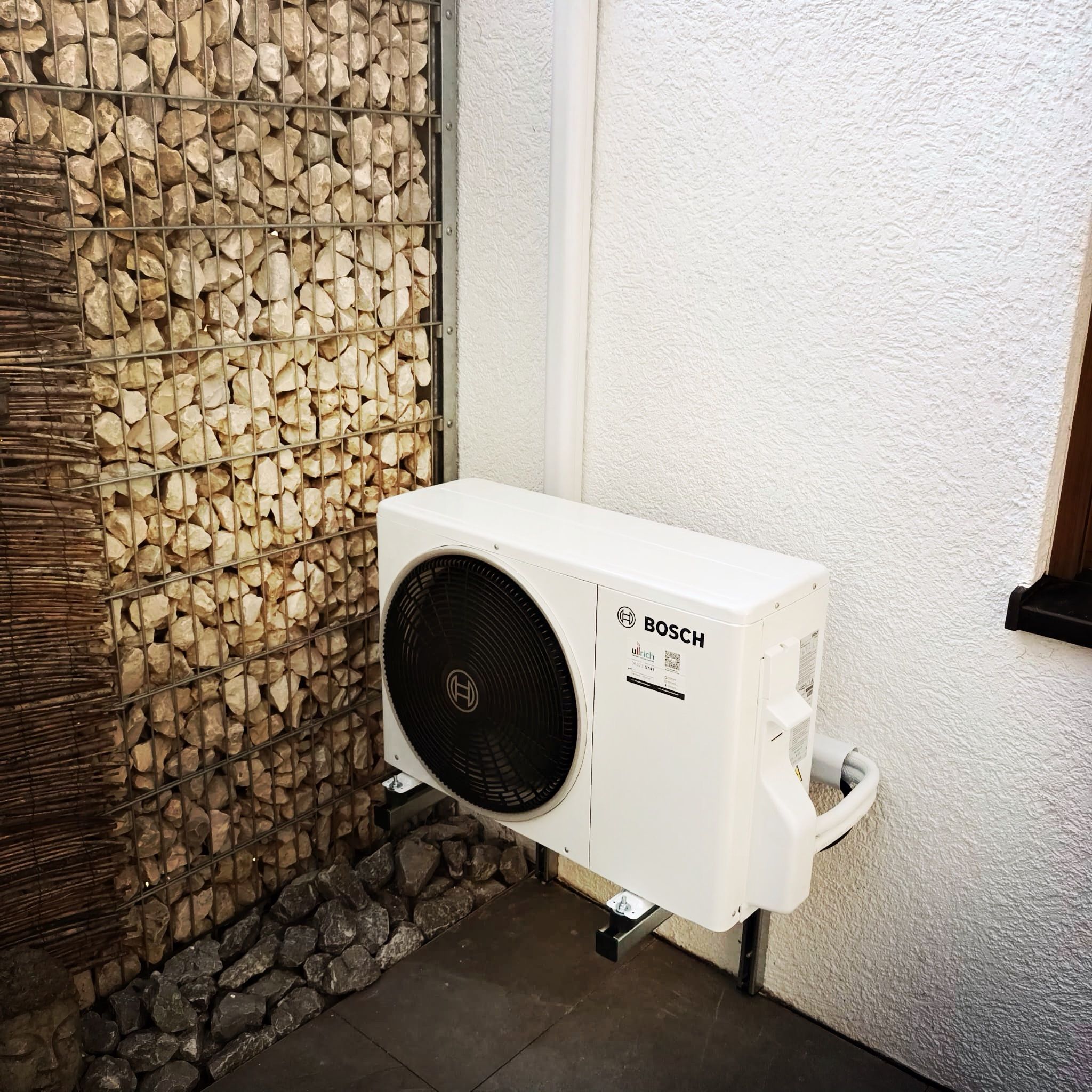 Bosch-Außengerät einer Klimaanlage auf einer Wandkonsole neben einer Gabionenwand