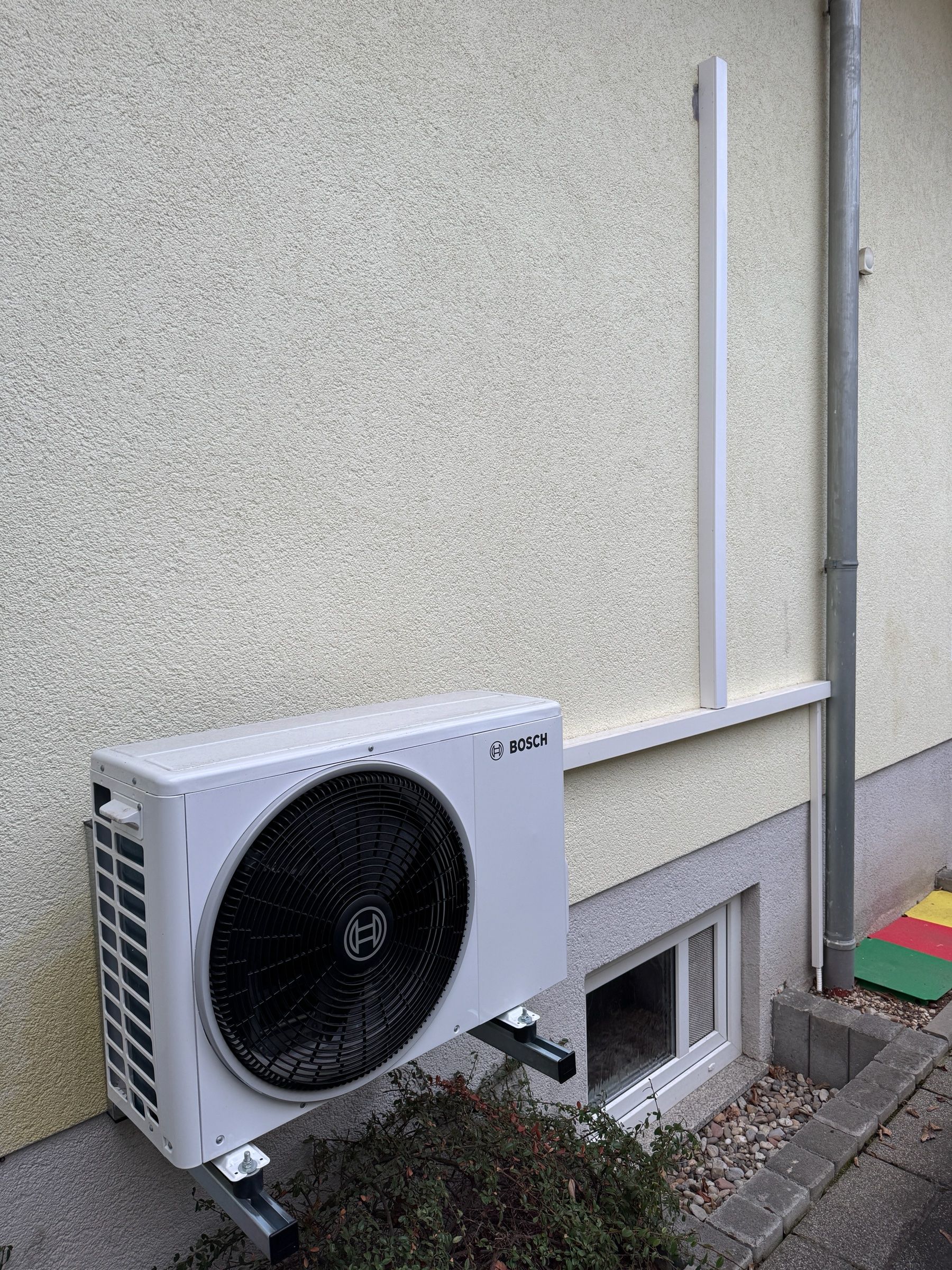 Bosch-Außengerät einer Klimaanlage auf einer Wandkonsole neben einem Kellerfenster