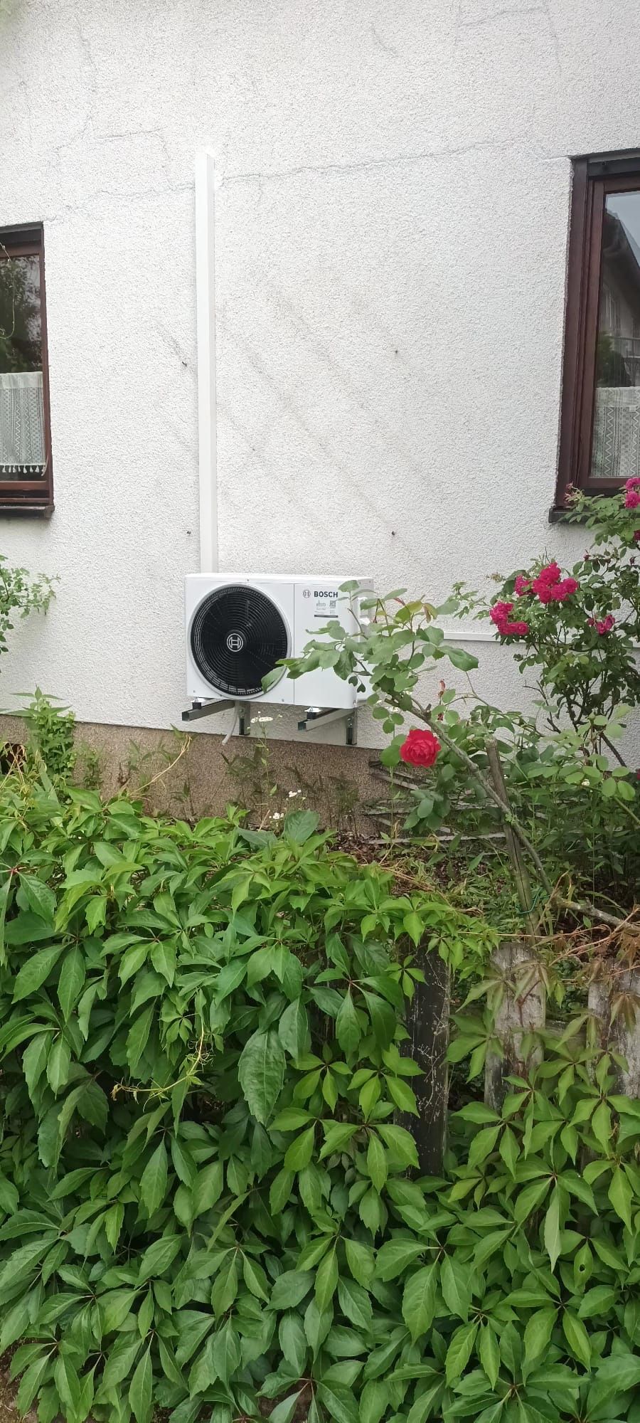 Kleines Außengerät einer Klimaanlage an einer Hauswand über einem bewachsenen Beet