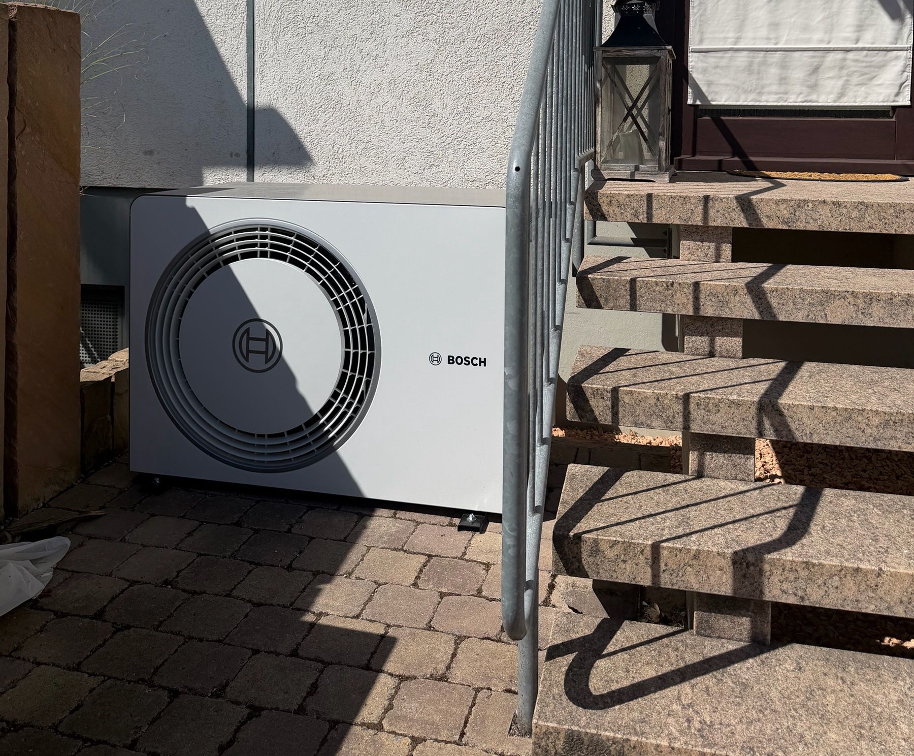 Außeneinheit einer Bosch-Wärmepumpe neben einer Steintreppe auf gepflastertem Boden