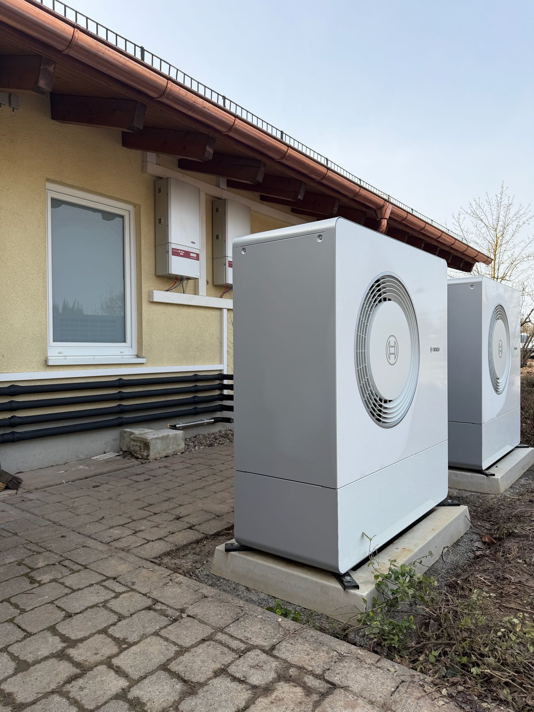 Zwei Außeneinheiten von Luft-/Wasser-Wärmepumpen auf Betonsockeln vor einem Wohnhaus