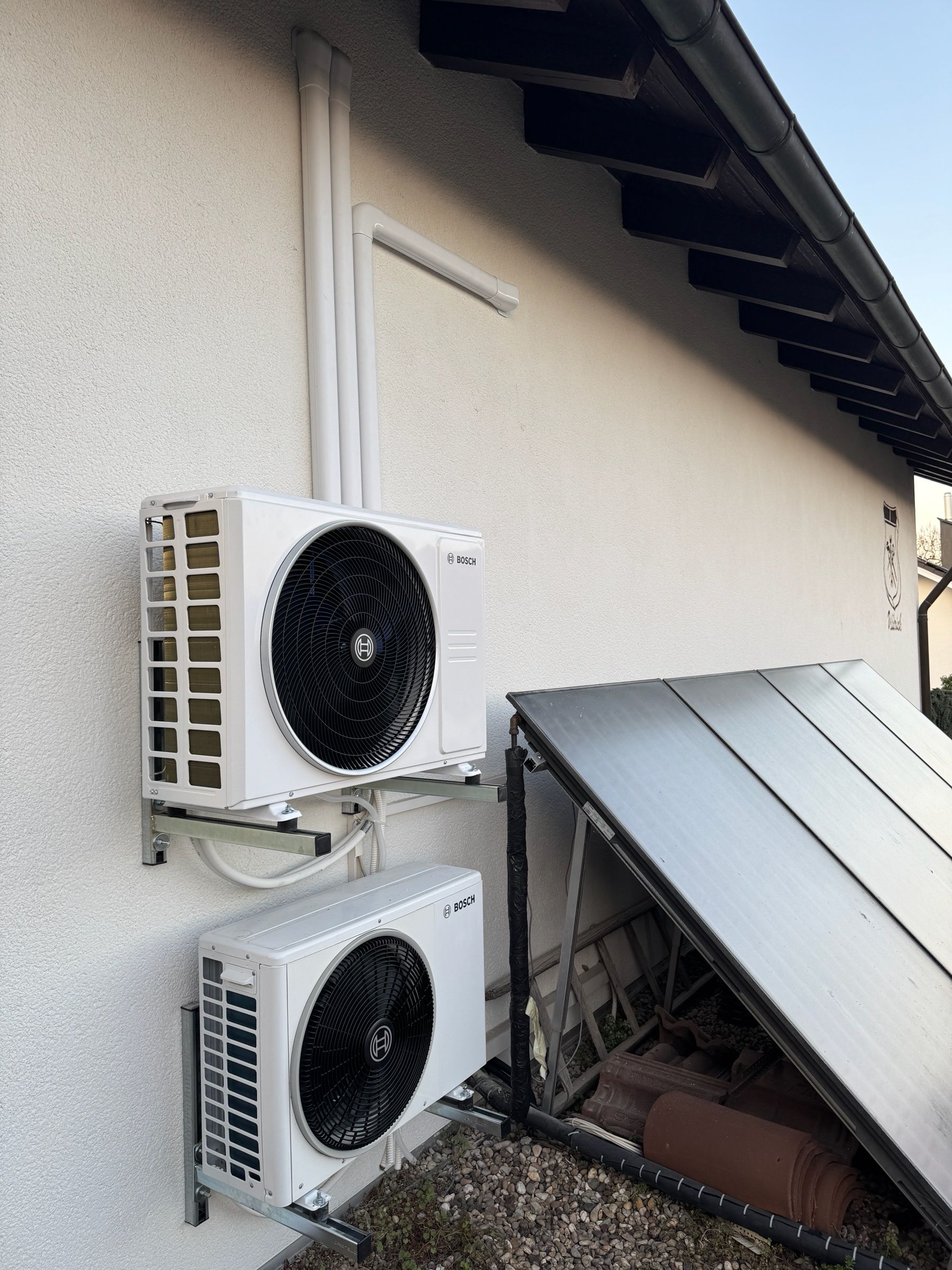 Zwei Bosch-Außengeräte einer Klimaanlage übereinander an einer Hauswand neben einem Solarpaneel