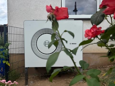 Außeneinheit einer Bosch-Wärmepumpe hinter roten Rosen vor einer hellen Hauswand
