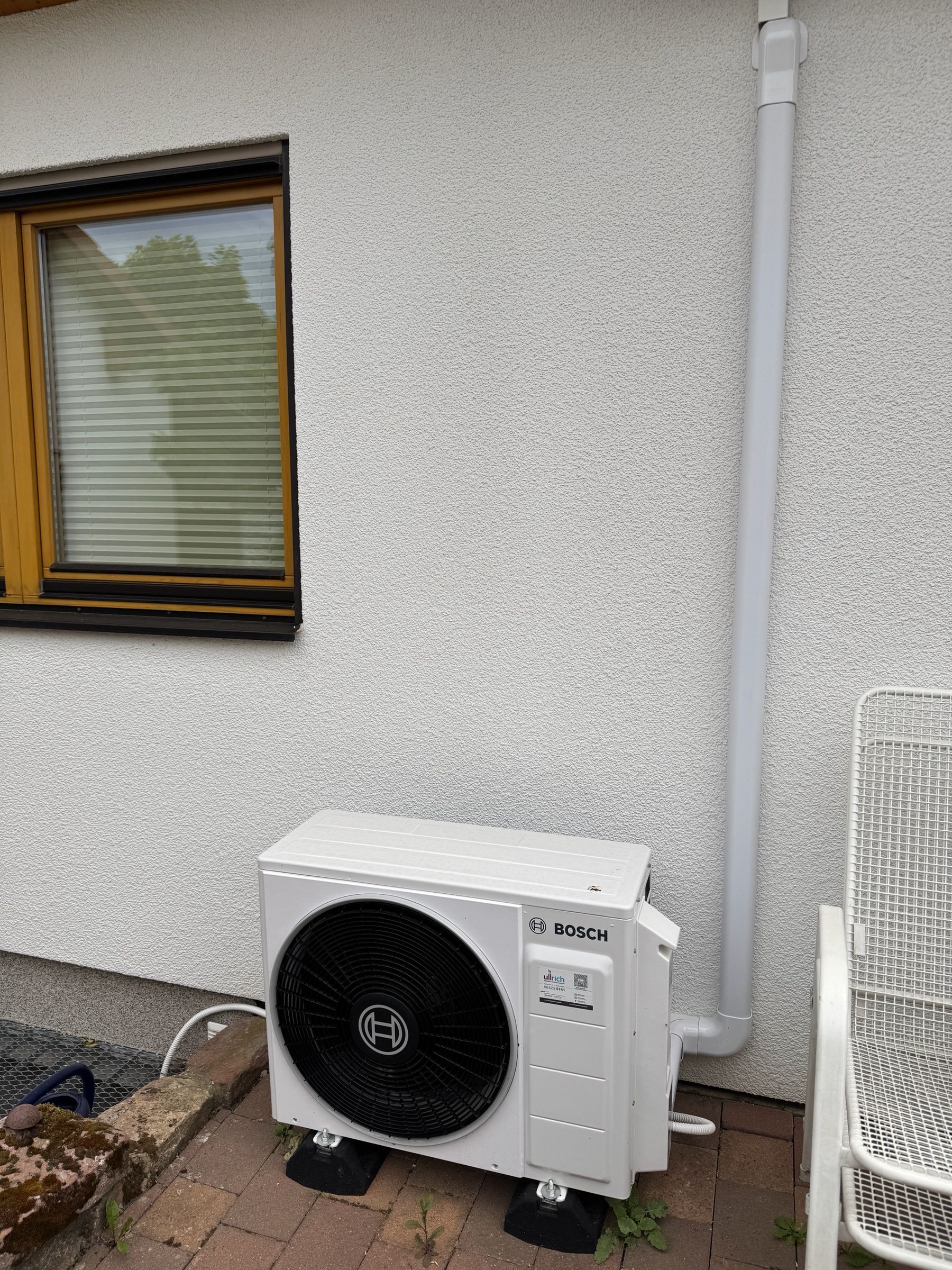 Bosch-Außengerät einer Klimaanlage auf Bodenfüßen neben einem Fallrohr