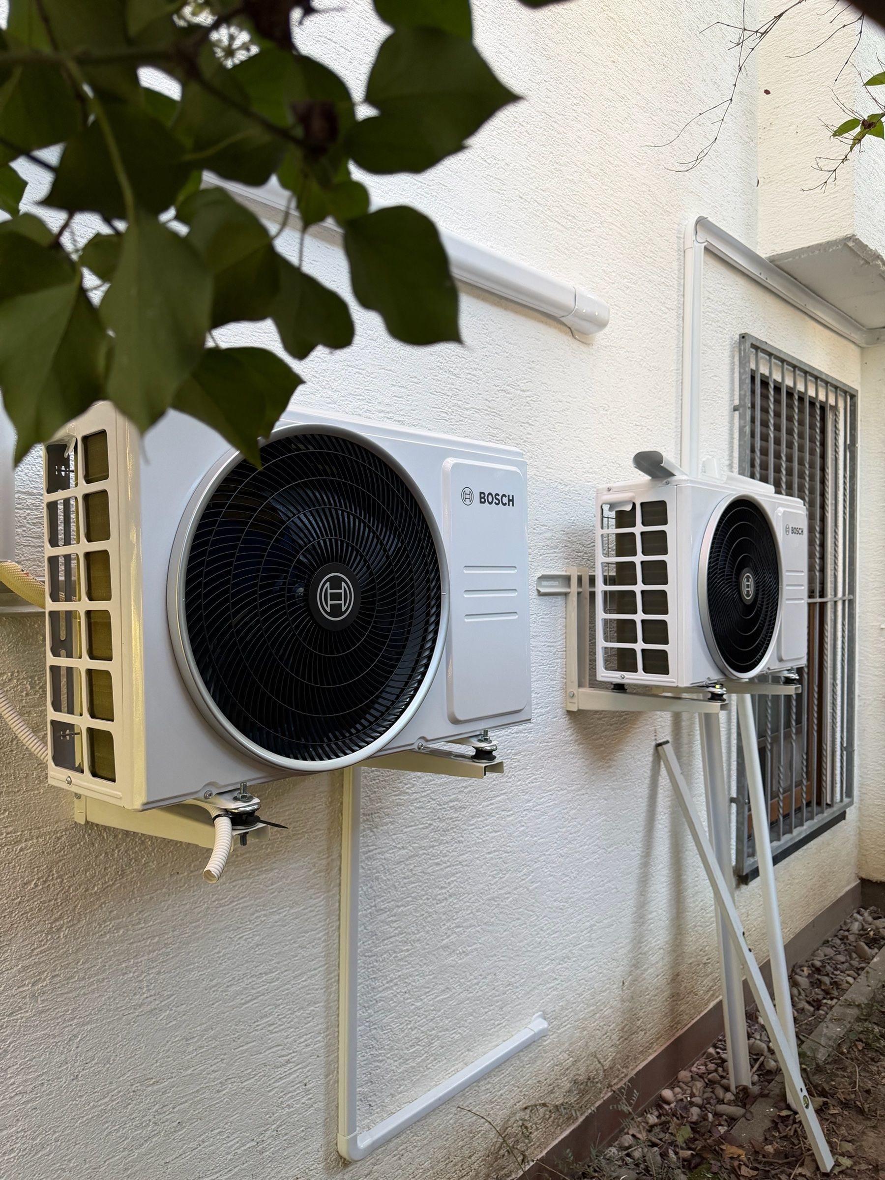 Zwei Bosch-Außengeräte einer Klimaanlage auf Wandkonsolen an einer weißen Hauswand