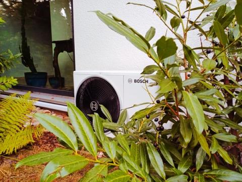 Bosch-Außengerät einer Klimaanlage zwischen Gartenpflanzen vor einer Glasfront