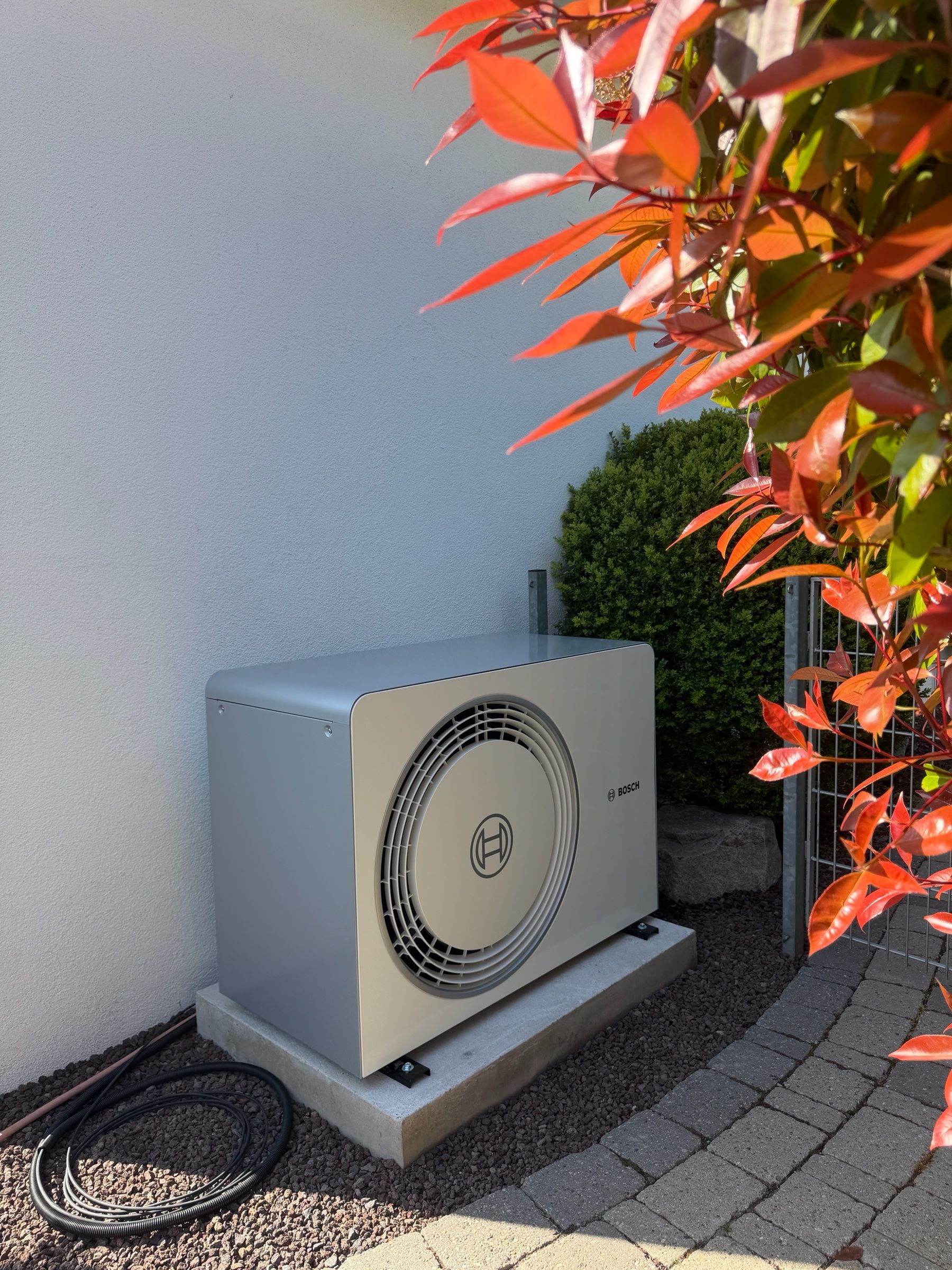 Außeneinheit einer Bosch-Wärmepumpe auf einem Betonsockel an einer weißen Hauswand