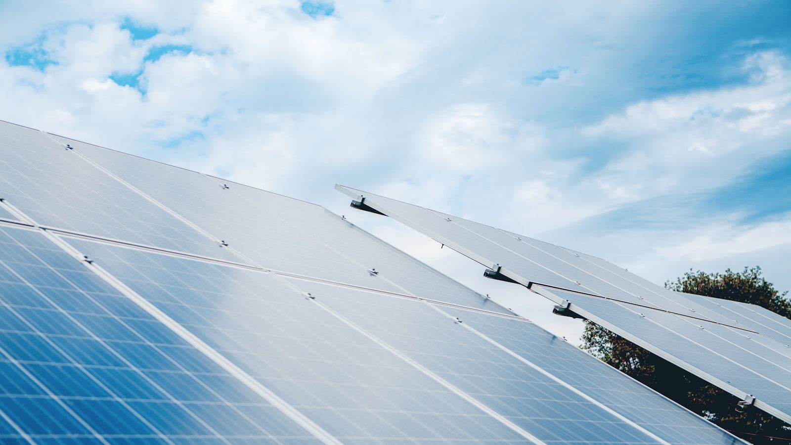 Rows of photovoltaic solar panels tilted under a cloudy sky — illustrating the optimum tilt angle