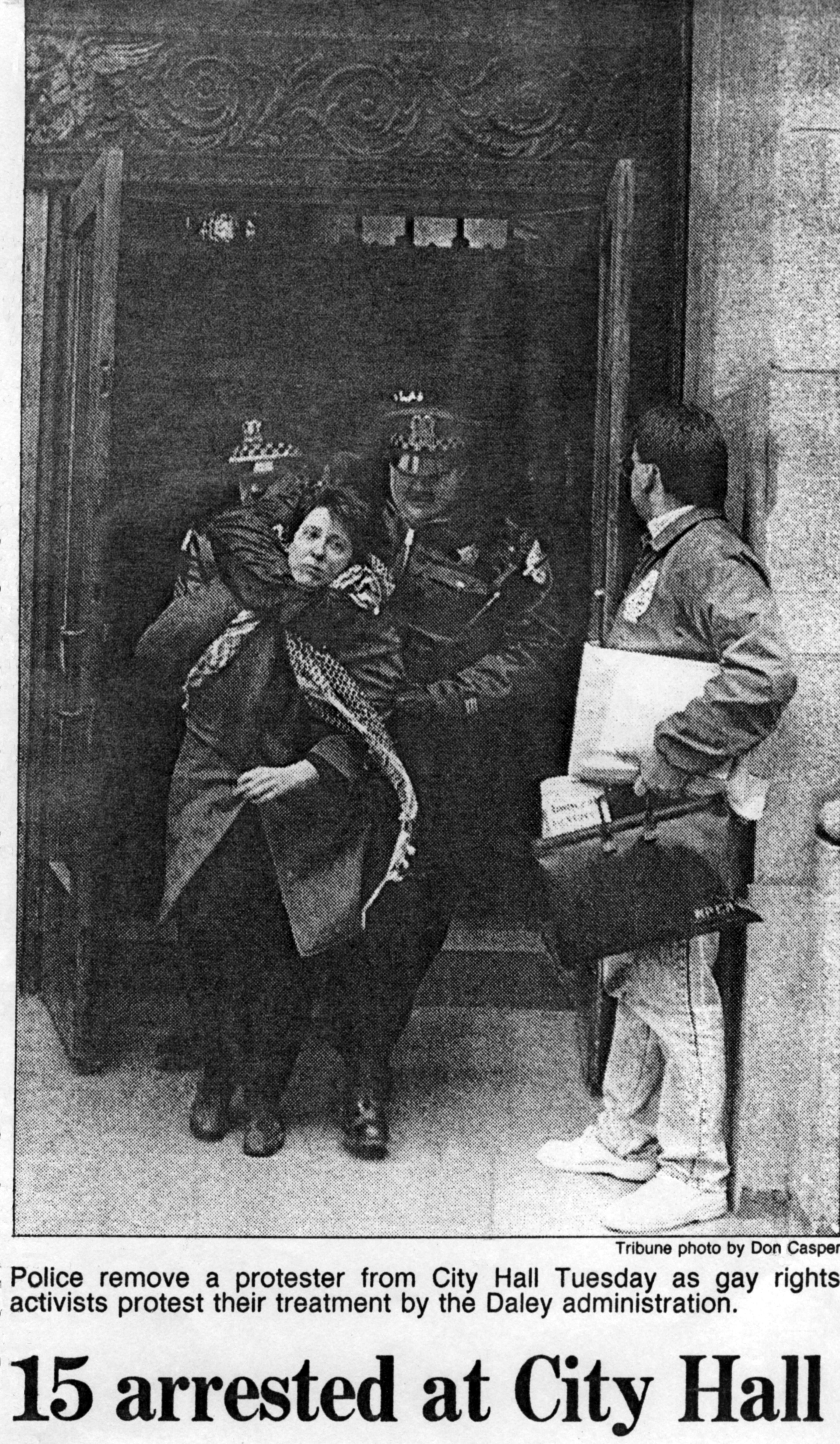 Black-and-white newspaper photo of Mary Patten being arrested at Chicago’s City Hall in November, 1989. On Patten’s left side is a large police office holding Patten’s head in a choke-hold, with another cop right behind. Patten is wearing a winter coat and a keffiyeh (Palestinian scarf). Her left hand grasps one edge of the coat inside which was $1,000 of bail money. The civil disobedience action was in protest of AIDS policies and discrimination by then-Mayor Richard M. Daley and his administration. On the right side of the photo is an unidentified man holding a briefcase and folders under his arm, watching the scene.