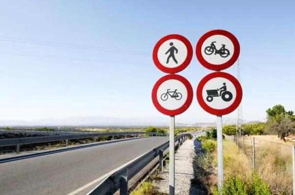 Cuatro señales restrictivas redondas que prohíben peatones, motocicletas, bicicletas y tractores junto a una autopista