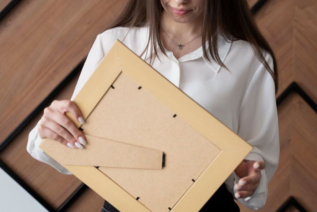 Mujer sostiene un marco de madera clara por el reverso, mostrando el soporte trasero