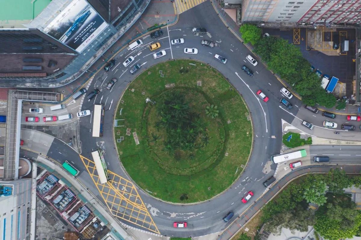 Vista aérea de una glorieta con centro de pasto y autos y autobuses circulando a su alrededor