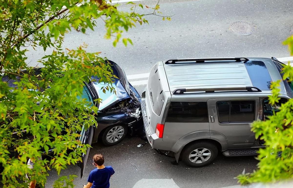 Vista desde arriba de un choque entre un auto azul y una camioneta gris en una calle, con una persona junto a ellos