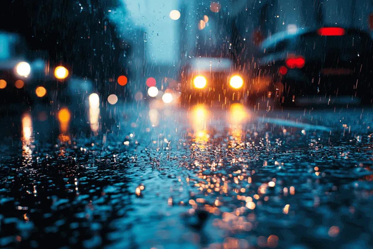Calle mojada de noche bajo la lluvia, con faros y luces de autos desenfocados reflejados en el pavimento