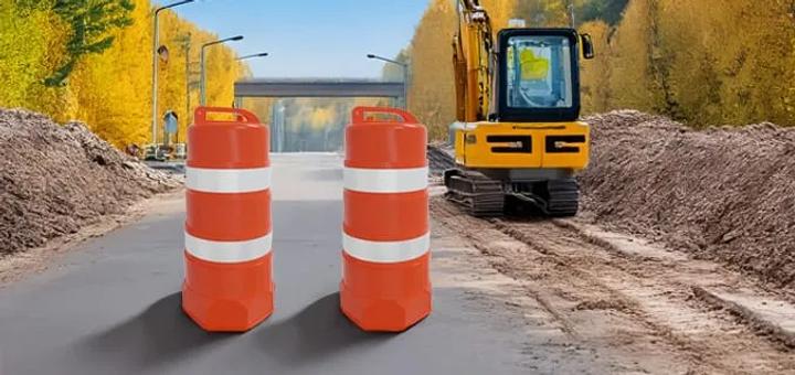 Dos trafitambos naranjas con bandas reflejantes blancas en un camino en obra, junto a una excavadora amarilla
