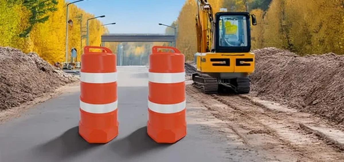 Dos trafitambos naranjas con bandas reflejantes blancas en un camino en obra, junto a una excavadora amarilla