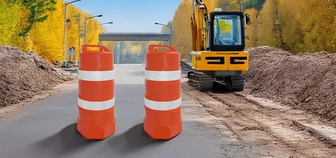 Dos trafitambos naranjas con bandas reflejantes blancas en un camino en obra, junto a una excavadora amarilla