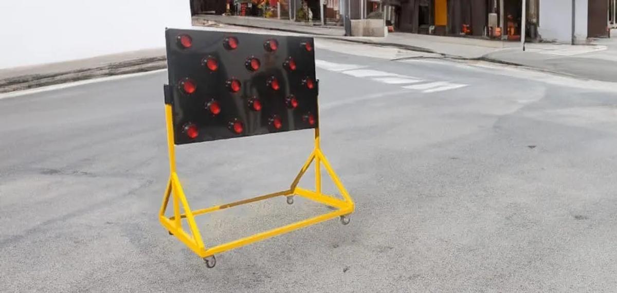 Flechero luminoso de panel negro con luces rojas sobre un soporte amarillo con ruedas en una calle