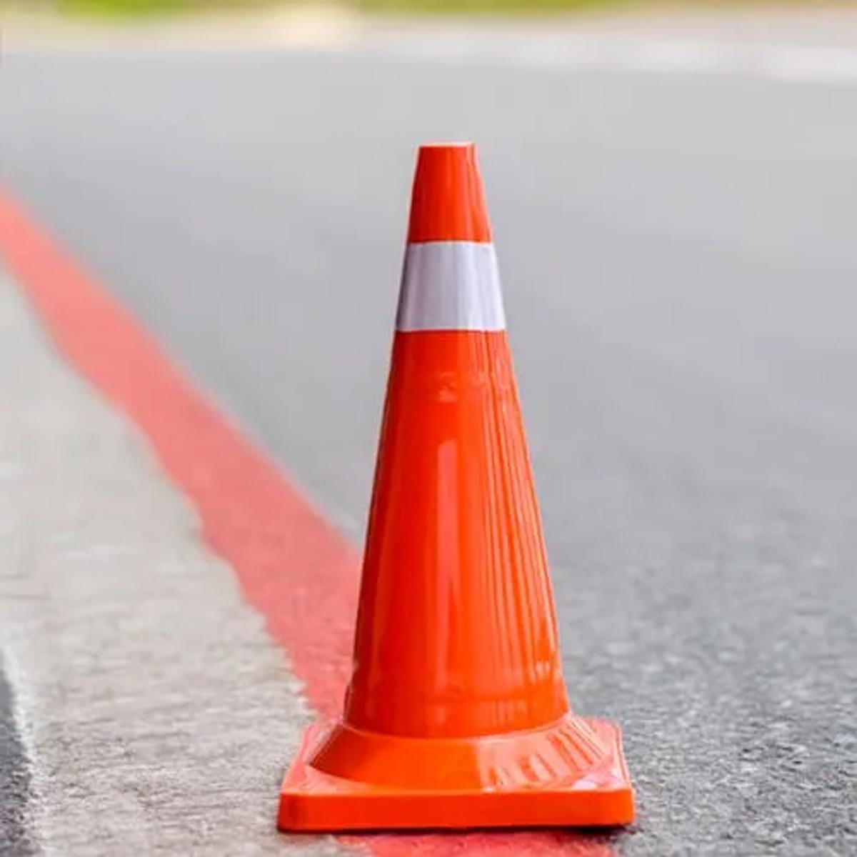 Cono vial naranja con una banda reflejante blanca sobre el asfalto, junto a una franja roja