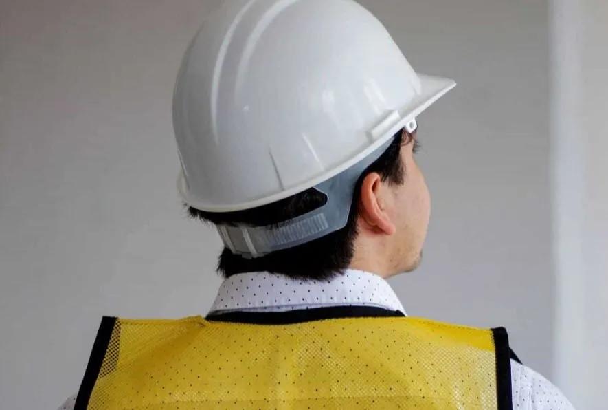 Trabajador de espaldas con casco de seguridad blanco y chaleco amarillo de malla