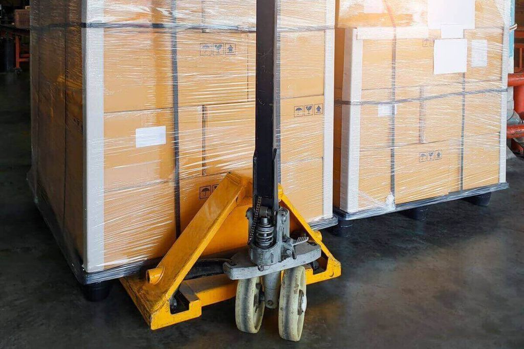 Dos tarimas de cajas emplayadas con un patín hidráulico amarillo al frente en un almacén