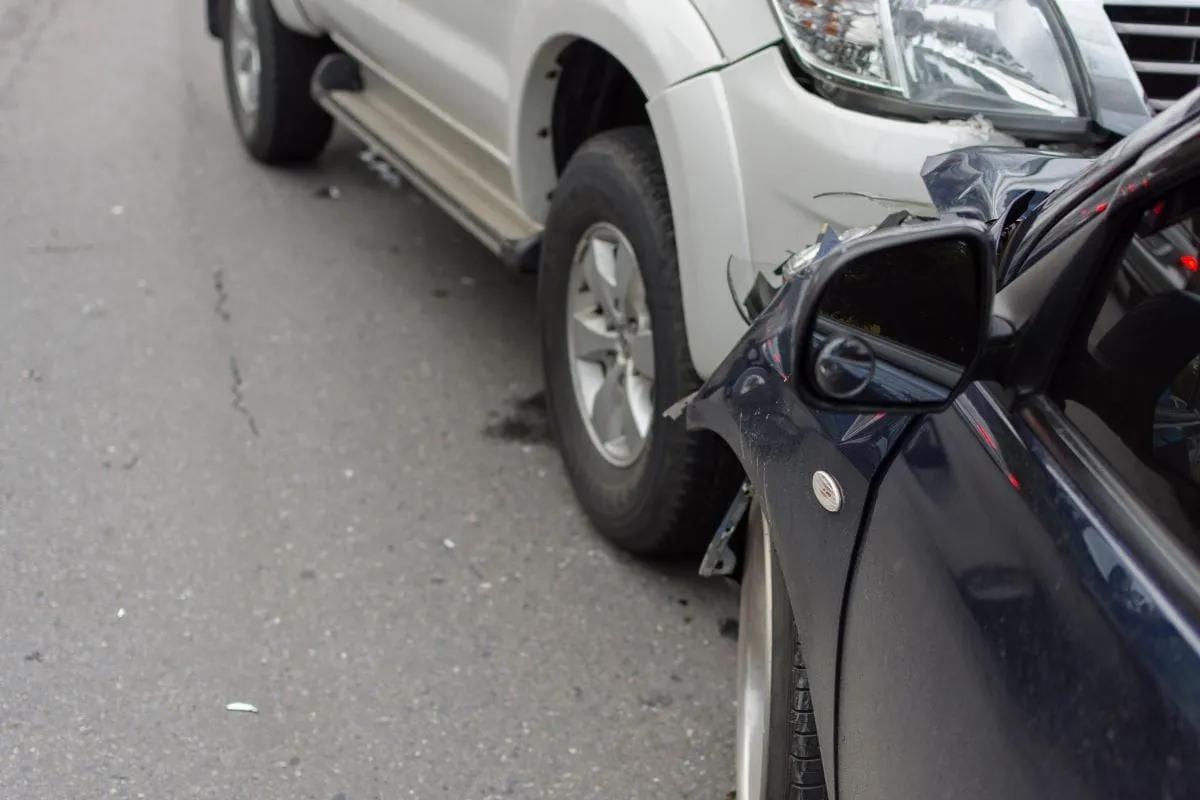Choque lateral entre una camioneta blanca y un auto azul oscuro sobre el asfalto, con el espejo dañado