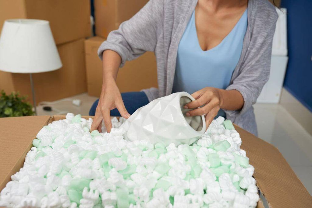 Mujer coloca un jarrón blanco geométrico en una caja llena de cacahuates de relleno blancos y verdes