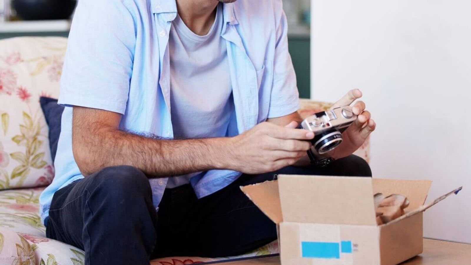 Hombre sonriente sentado en un sillón sostiene una cámara fotográfica recién sacada de una caja de cartón abierta