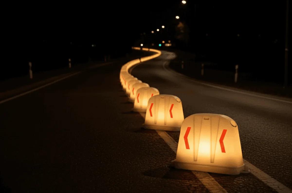 Hilera de barreras anidables con luz encendida y flechas rojas que marcan una curva en una carretera de noche