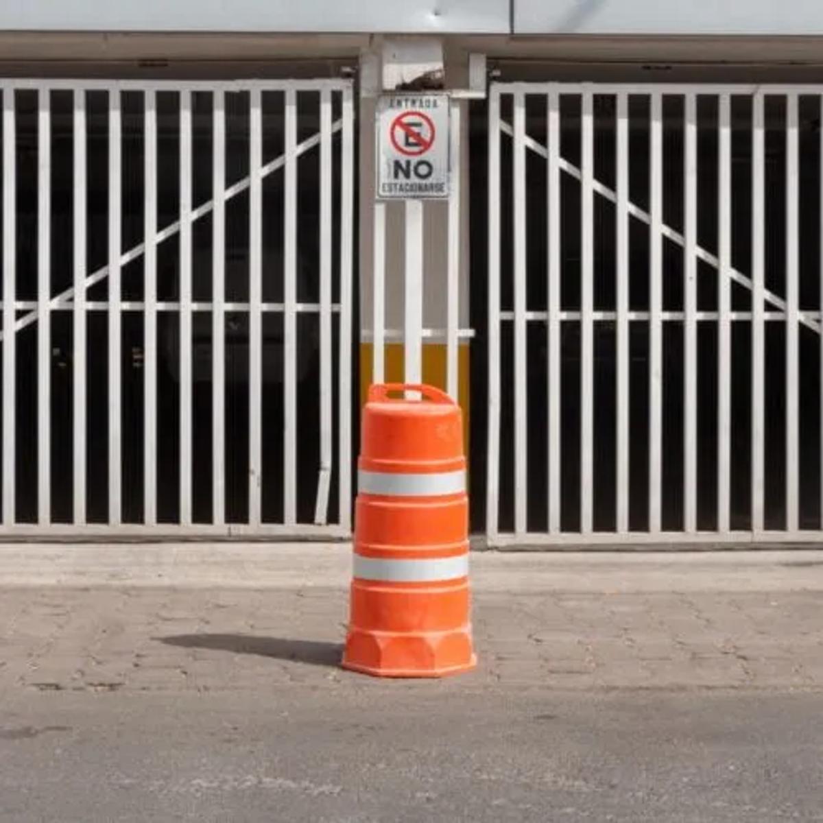 Trafitambo naranja con dos bandas reflejantes frente a un portón blanco con letrero de no estacionarse