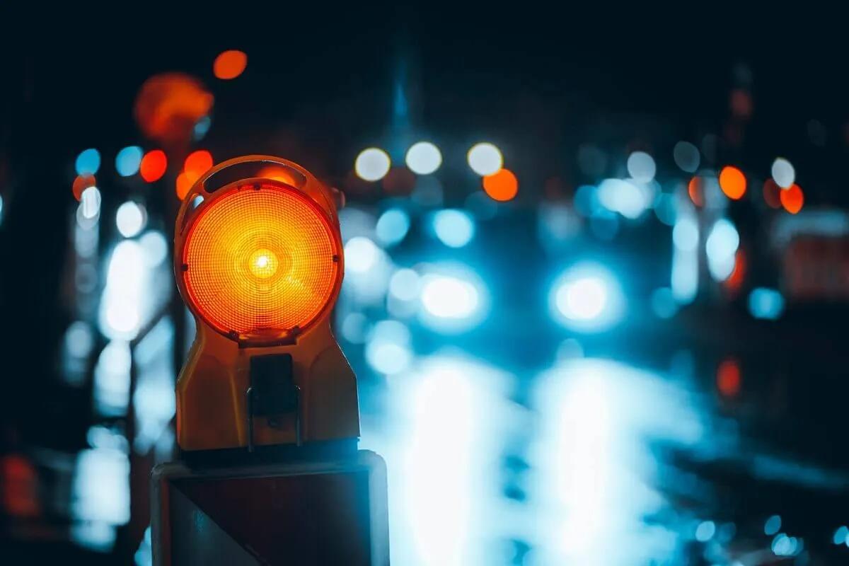Lámpara de destello ámbar encendida sobre una barrera en una calle de noche, con luces de autos desenfocadas