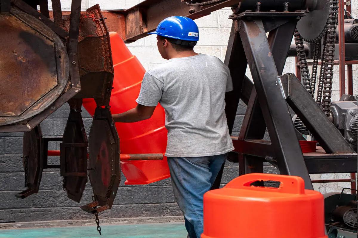 Operario con casco azul manipula un trafitambo naranja junto a una máquina de moldeo en la planta