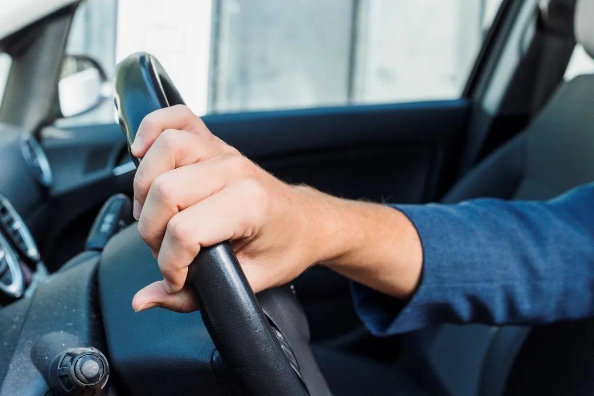 Mano de un conductor con manga azul sujeta el volante de un auto