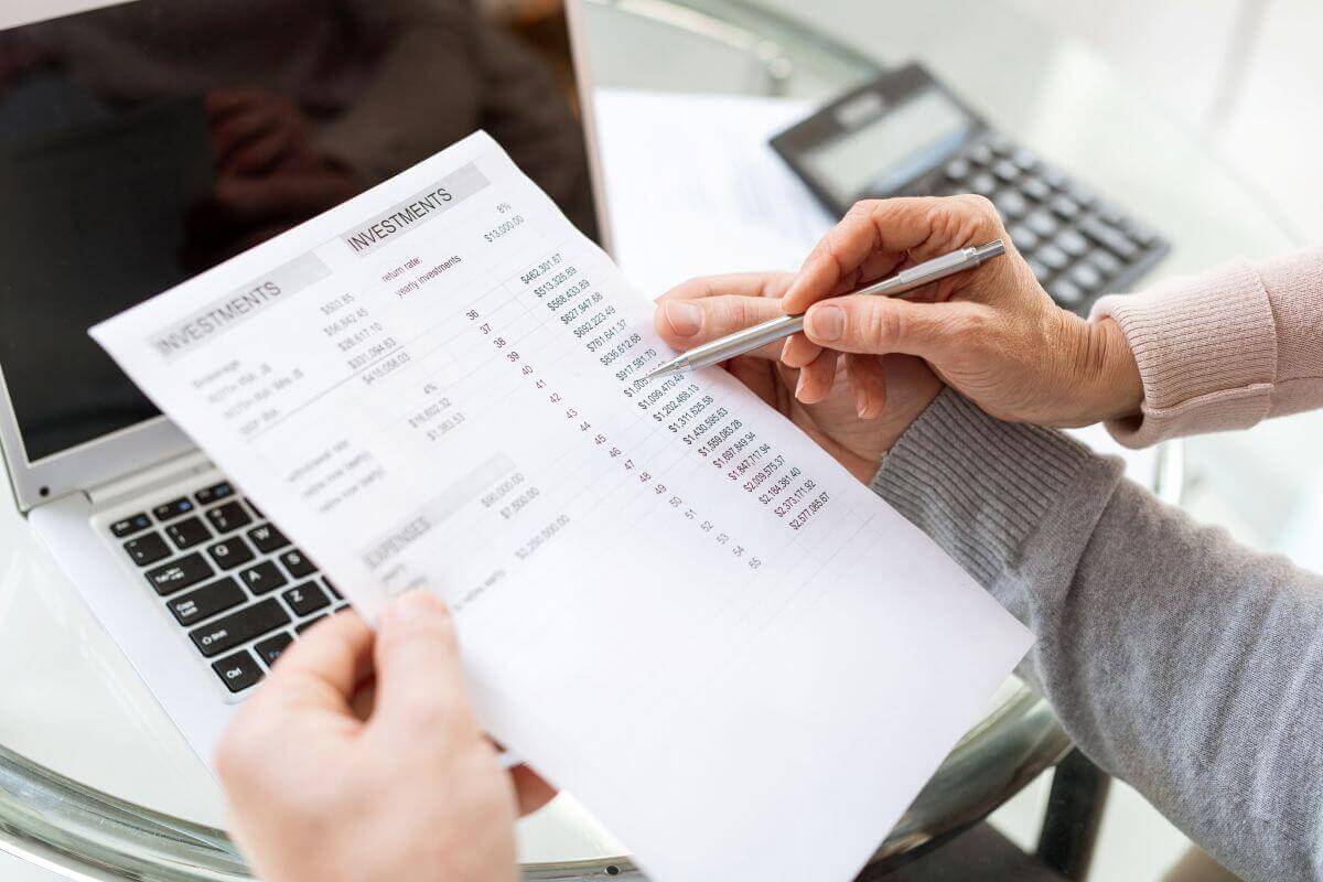 Dos personas revisan un documento de 'INVESTMENTS' con cifras financieras junto a una laptop y calculadora