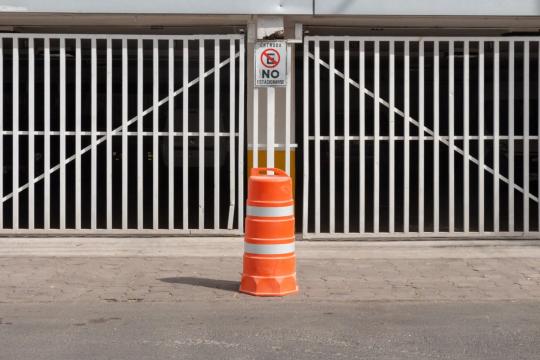 Trafitambo naranja con dos bandas reflejantes blancas frente a un portón blanco con letrero de no estacionarse