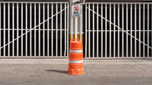 Trafitambo naranja con dos bandas reflejantes blancas frente a un portón blanco con letrero de no estacionarse