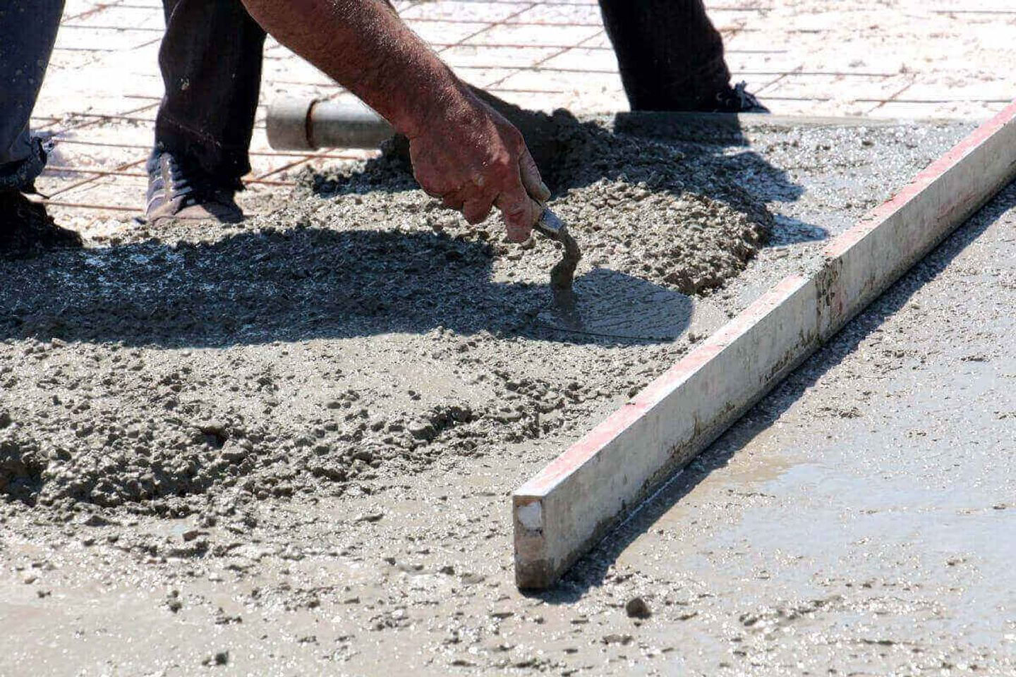 Trabajador extendiendo concreto fresco con llana sobre una superficie con varillas de refuerzo