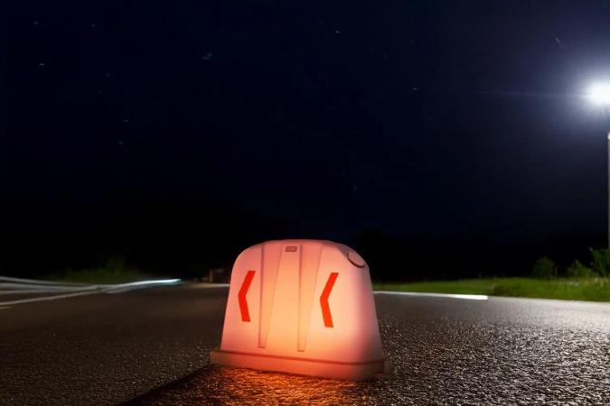 Barrera anidable con luz encendida de noche en el borde de una carretera, con un poste de alumbrado al fondo