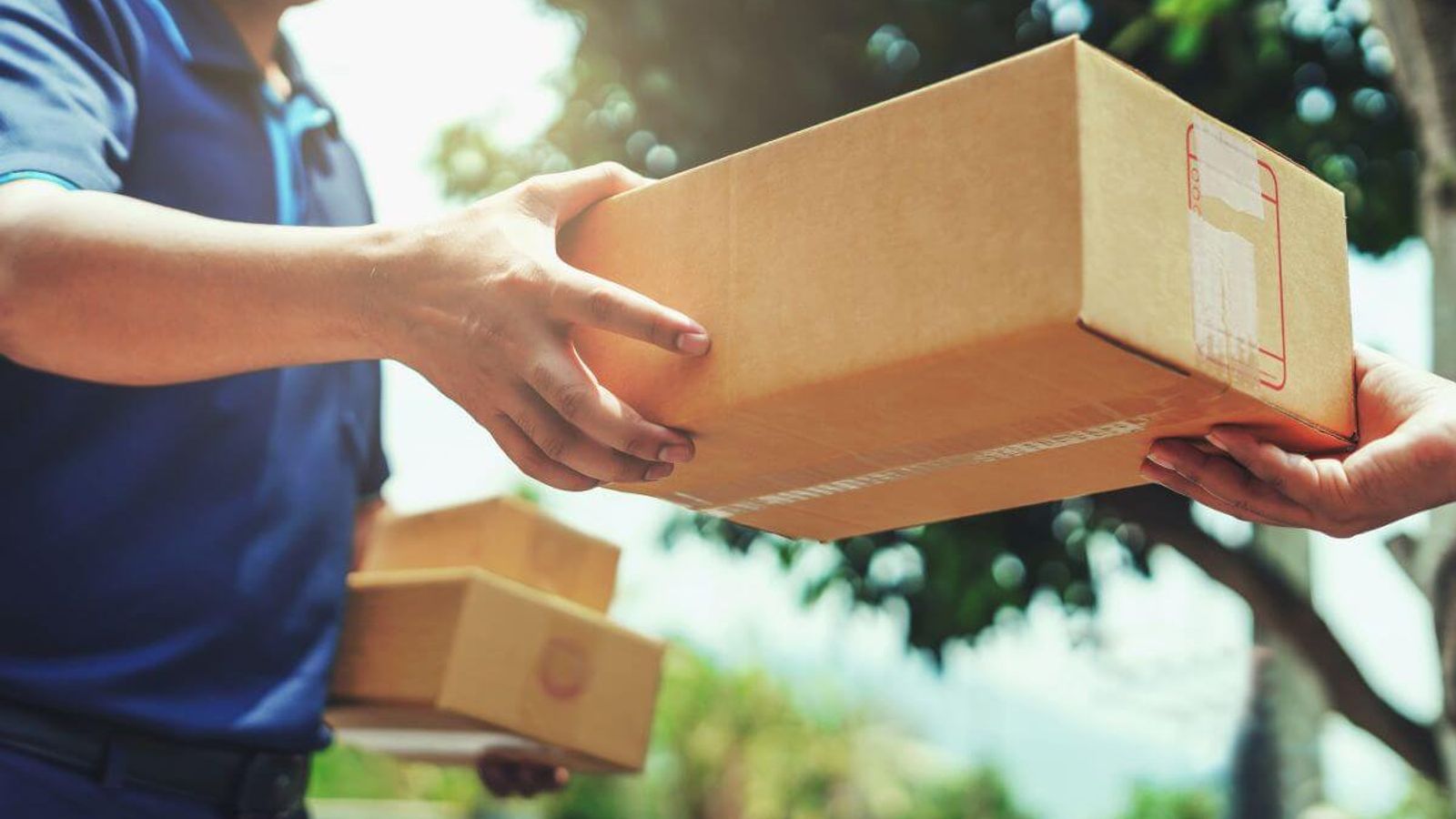 Repartidor de camisa azul entrega una caja de cartón en las manos de un cliente al aire libre